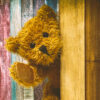 A teddy bear peaks out from behind a door and waves